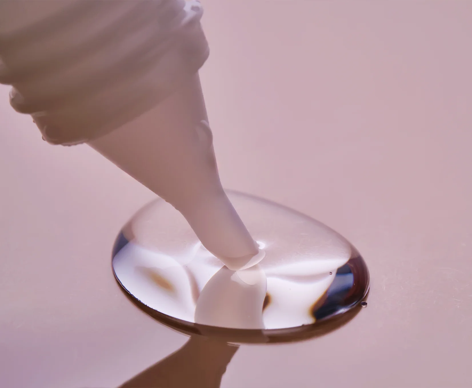 Nahaufnahme einer Dosierspitze, die eine klare, gelartige Flüssigkeit auf eine glatte, reflektierende Oberfläche aufträgt.