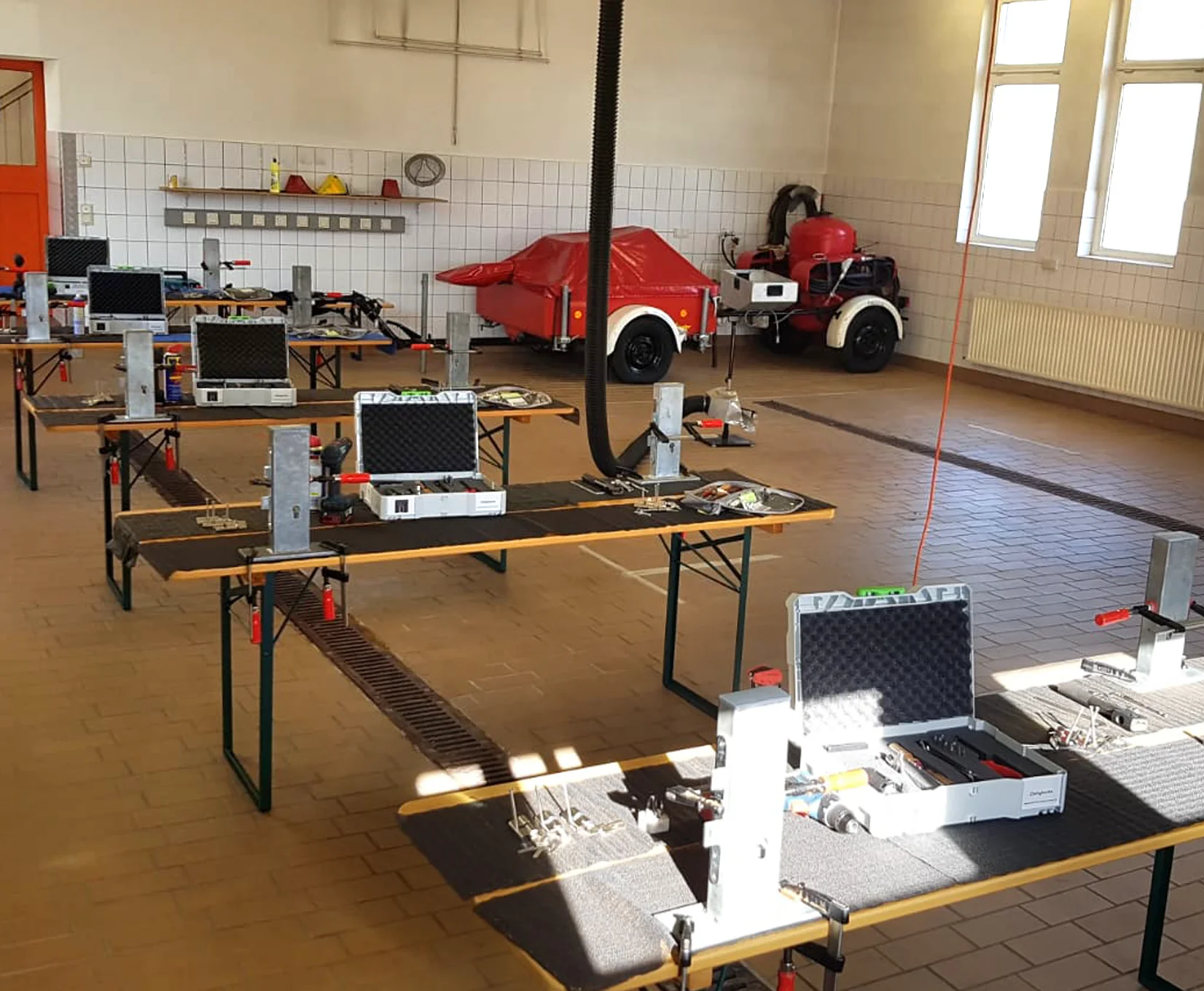 Schulungsraum mit mehreren Arbeitstischen, montierten Übungstüren, Werkzeugkoffern und Trainingsstationen für Tür- und Schließtechnik.