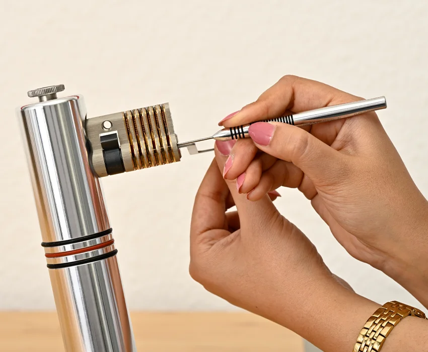 Hände verwenden einen Lockpick und einen Spanner an einem transparenten Trainingszylinder auf einem Übungsständer.