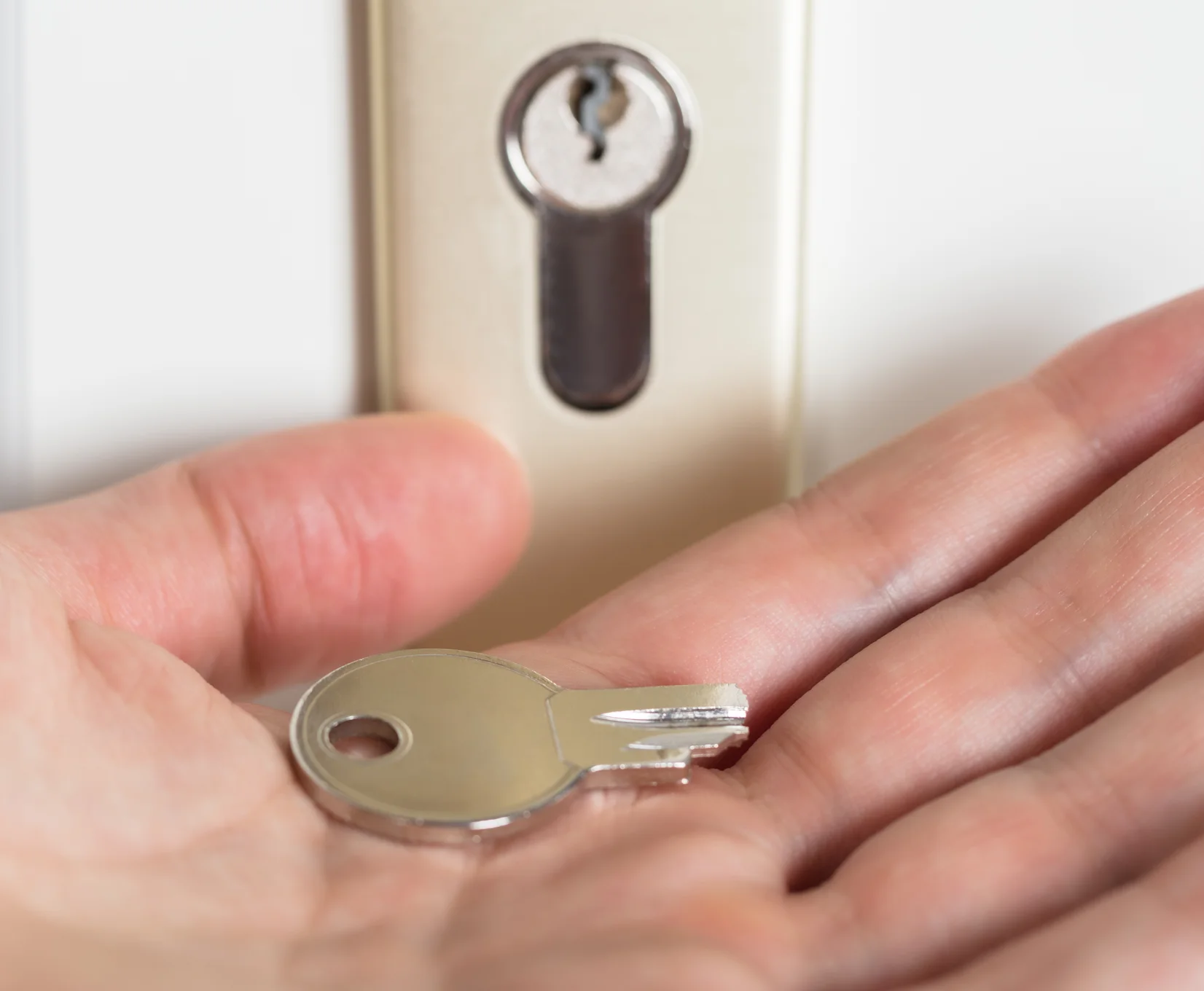 Hand holding a house key in front of a door lock