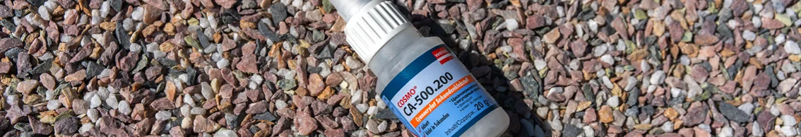 Kleine Kunststoffflasche mit Sekundenkleber liegt auf grobem Kies im Außenbereich