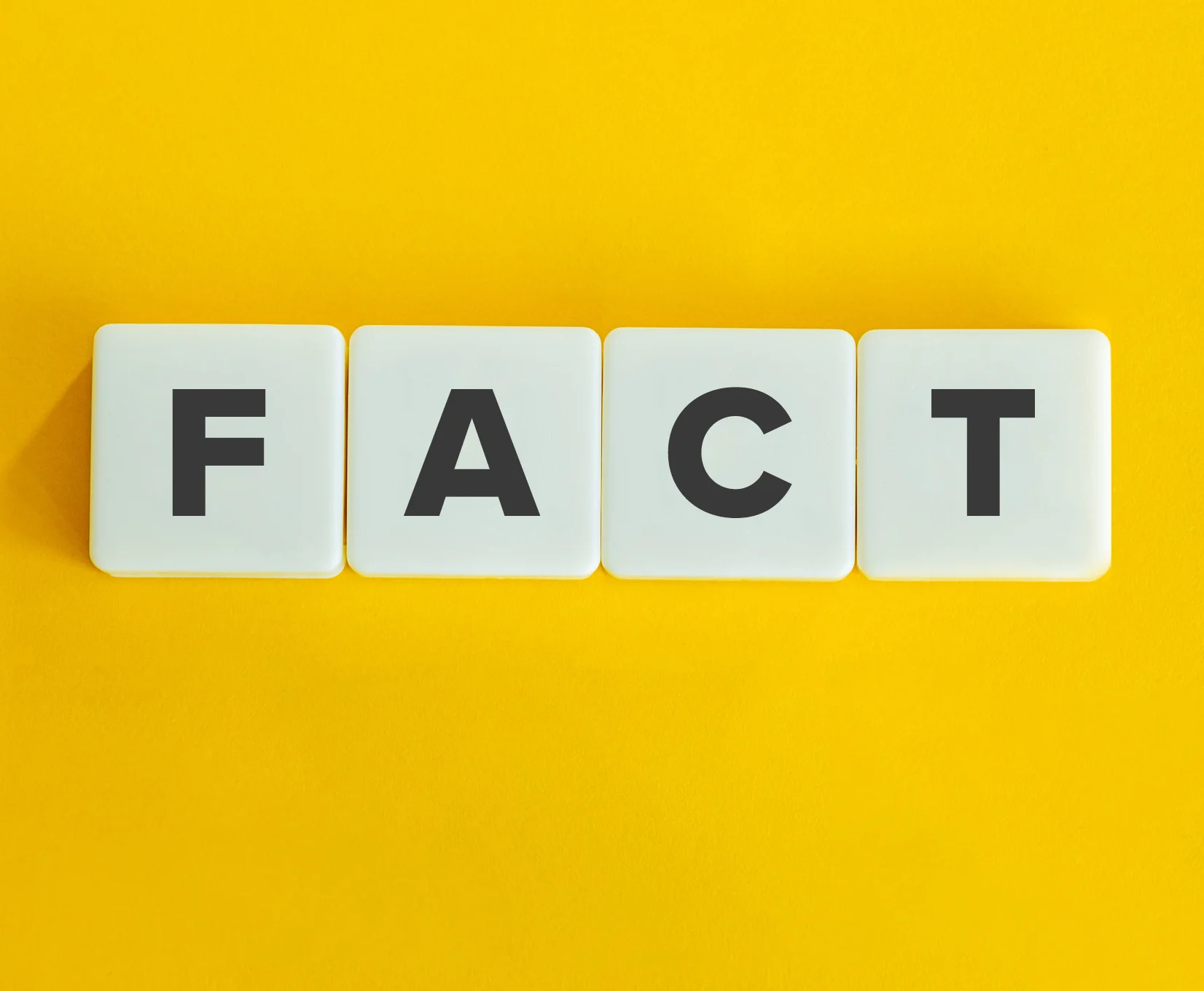 Mot “FACT” écrit sur des tuiles blanches sur fond jaune