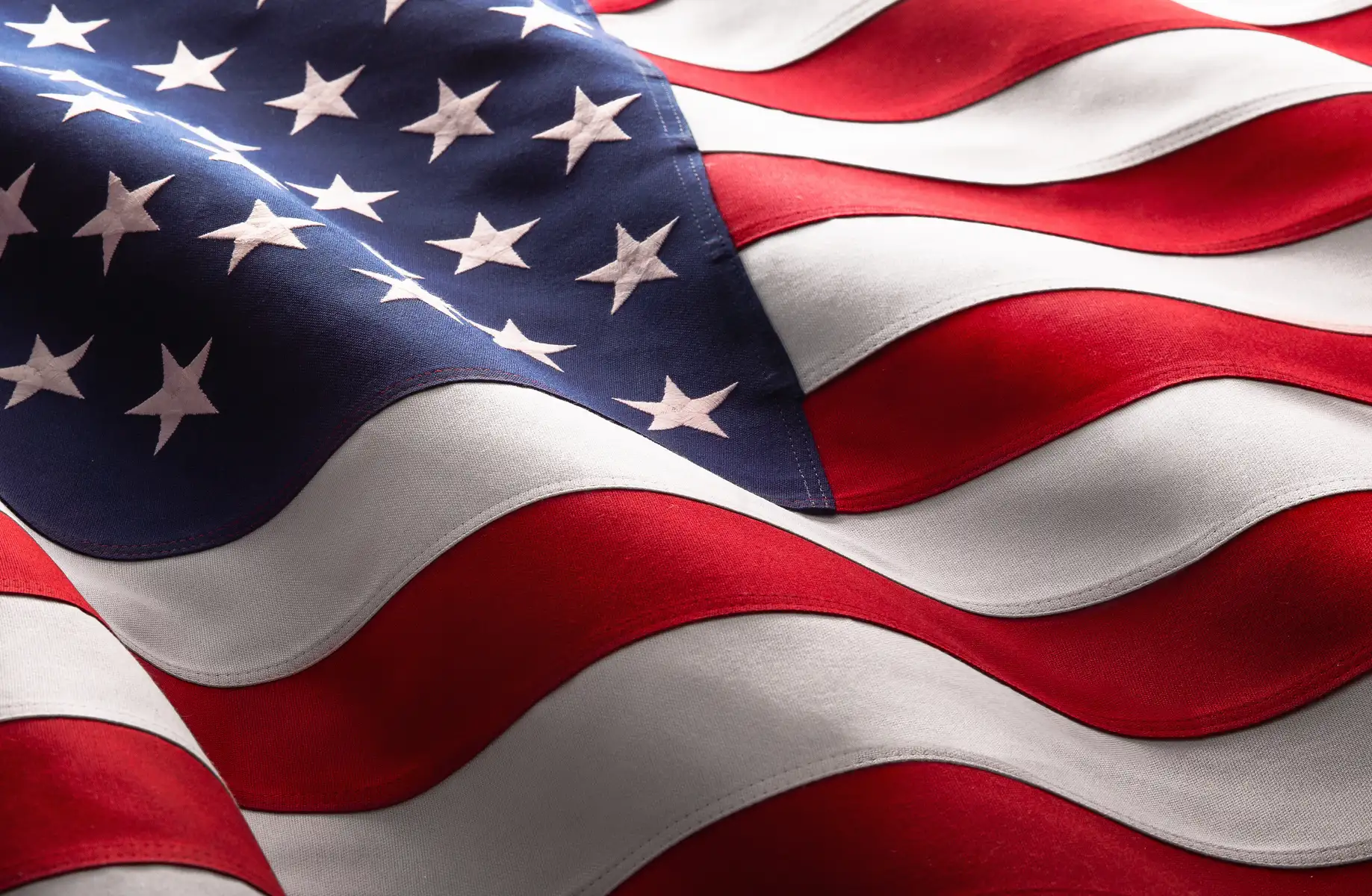 Nahaufnahme einer US-Flagge mit sichtbarer Stoffstruktur, weißen Sternen und geschwungenen roten und weißen Streifen.