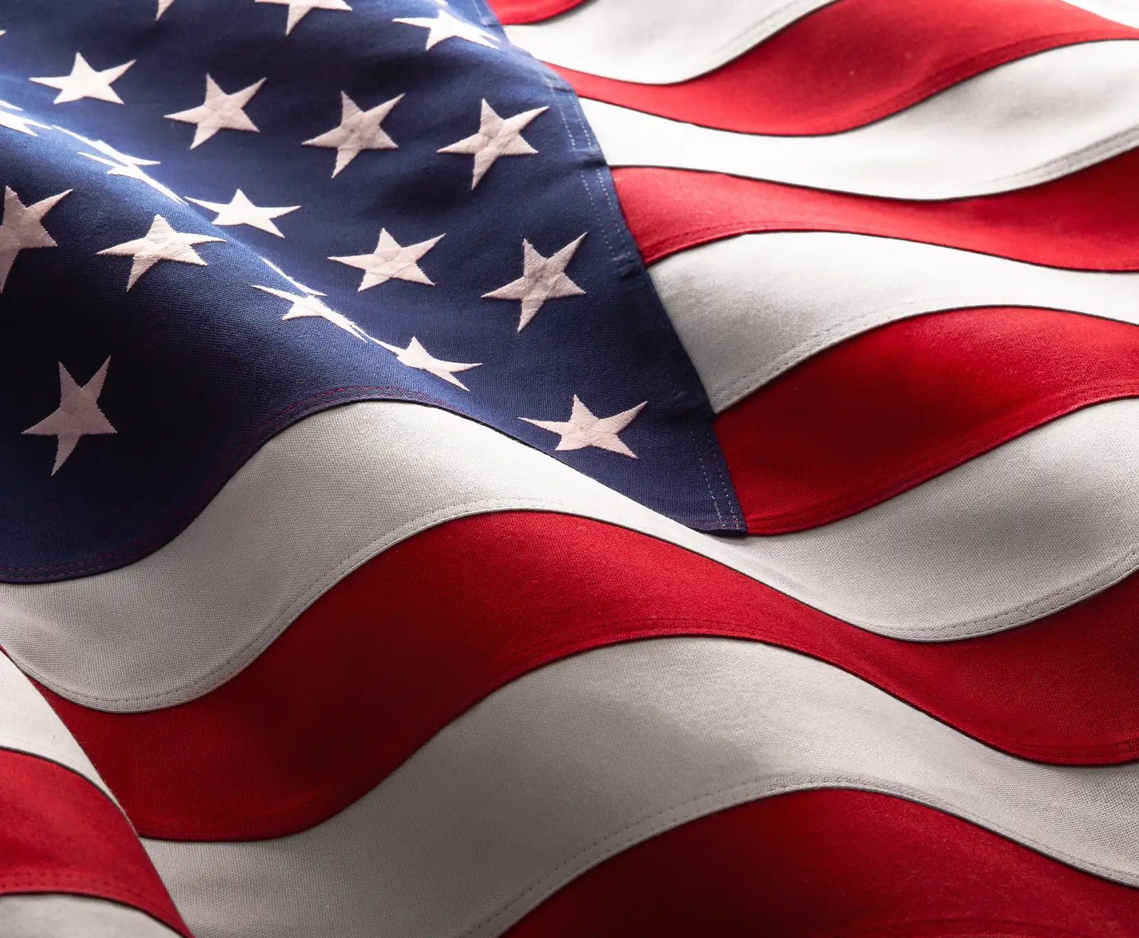 Nahaufnahme einer wehenden US-amerikanischen Flagge mit Sternen und roten sowie weißen Streifen auf strukturiertem Stoff.