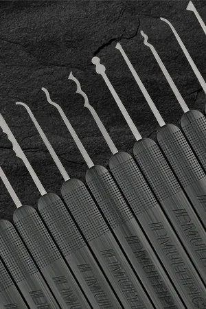 Several precision lock picks with black textured handles arranged in a row on a dark surface.