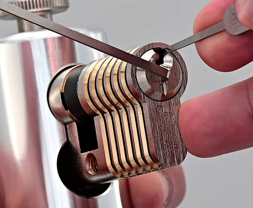 Nahaufnahme eines Europrofilzylinders, der mit einem Lockpick und einem Spanner auf einem Trainingsständer bearbeitet wird.